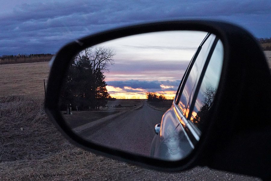 Auto Insurance - Close Up of Driver Side Review Mirror Showing a Road with a Sunset in the Distance