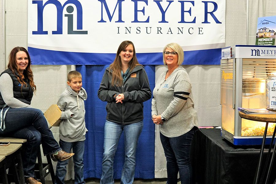 About Pages - Meyer Insurance Team at an Event with the Logo on the Banner Behind Them with a Popcorn Machine Beside them